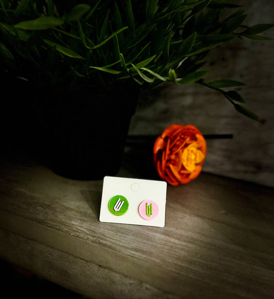 Small stud earrings with icons on a wooden surface next to a decorative orange flower.