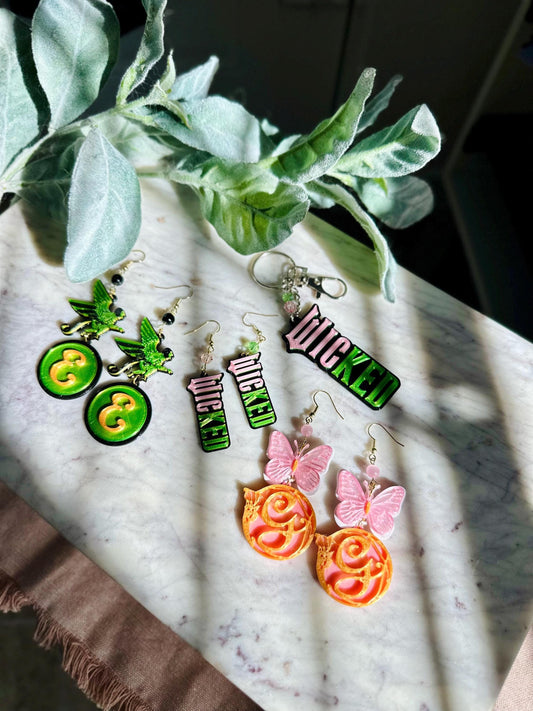 Wicked earrings, Green monkey tiered with Elphaba logo. Butterfly paired with gold pink Glinda Shiz logo